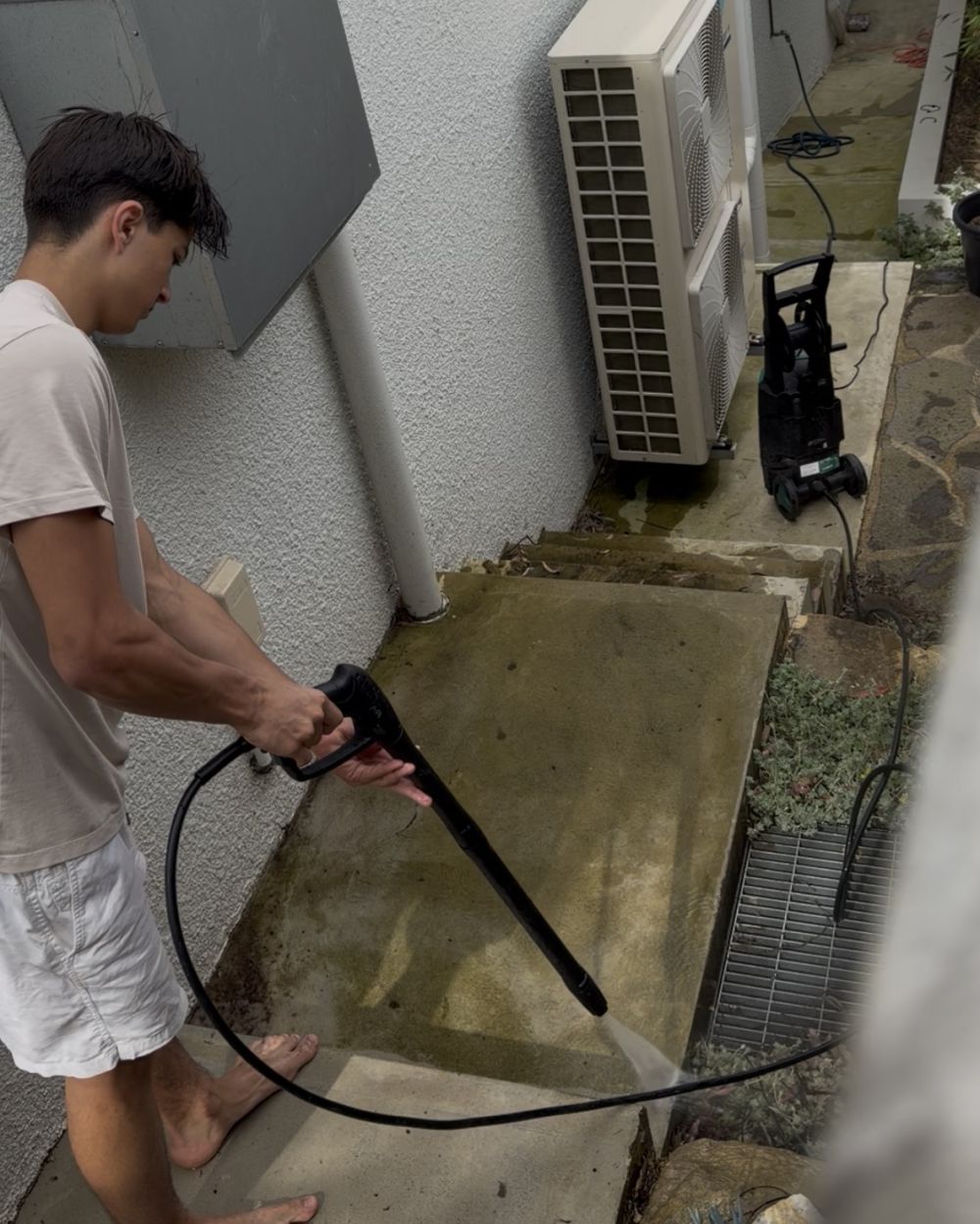 Sachin pressure washing a mossy concrete side path
